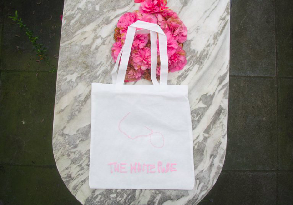 a white bag with the original white pube logo on in pink photographed on a marble table