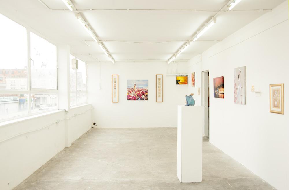 a white cube exhibition space with household decor including mass-produced paintings, framed art, and a statue of a wizard on a plinth