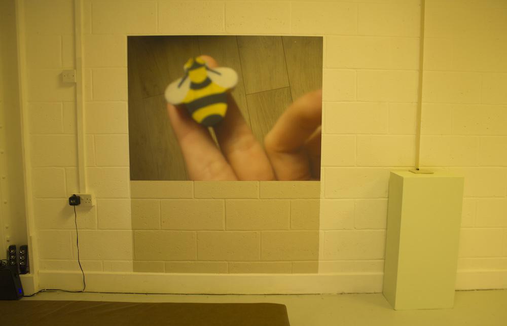 a print on the wall shows a rubber of a bumble bee at the end of two fingers, and below it, gab has painted the wall so the shape continues downwards in a beige colour