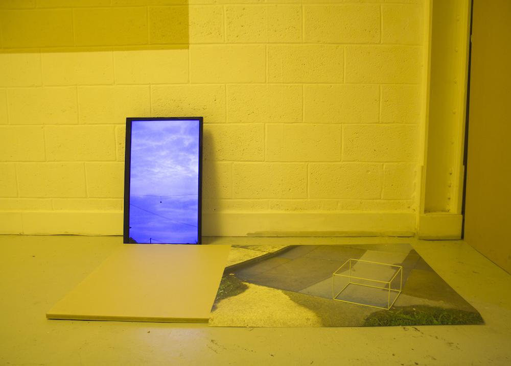 there is a vertical screen showing shoes hanging off a phone wire against a lilac sky, above wood, a big print of a puddle on the floor, and a mint green spray painted metal cube