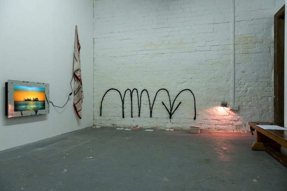 an illuminated picture on a wall, fabric hanging next to it, and arrows spray-painted in bouncing curves pointing down towards something on the ground