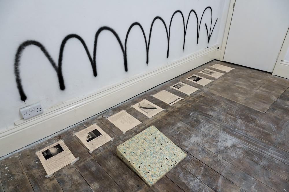 more spray painted bouncey arrows pointing down at essays printed on the floor with a foam piece that can be moved along the floor as you kneel to read