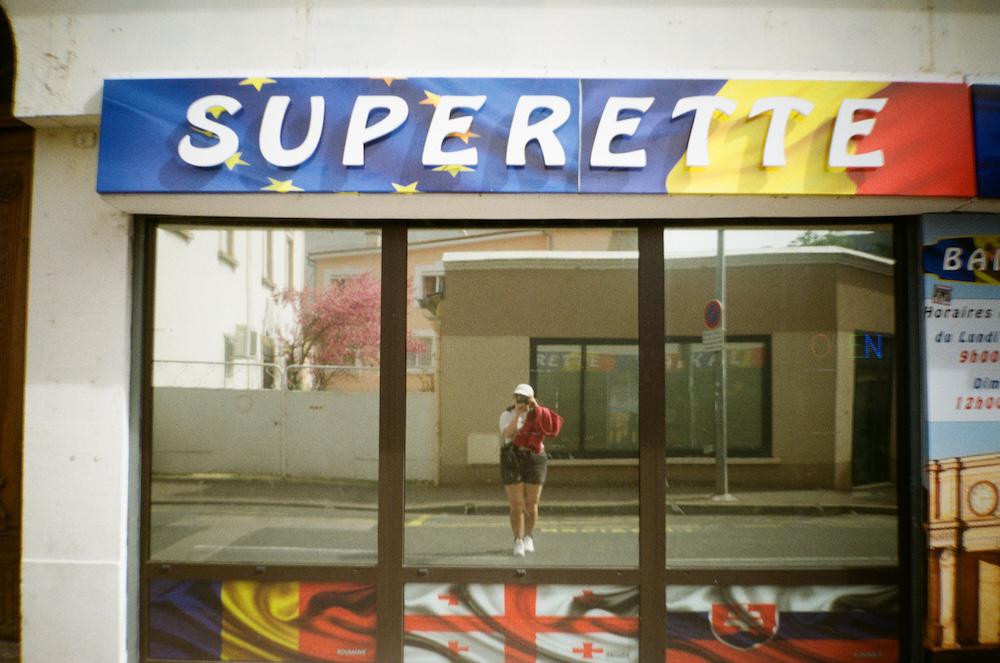 gab taking a picture in a reflective window of a supermarket in beziers france