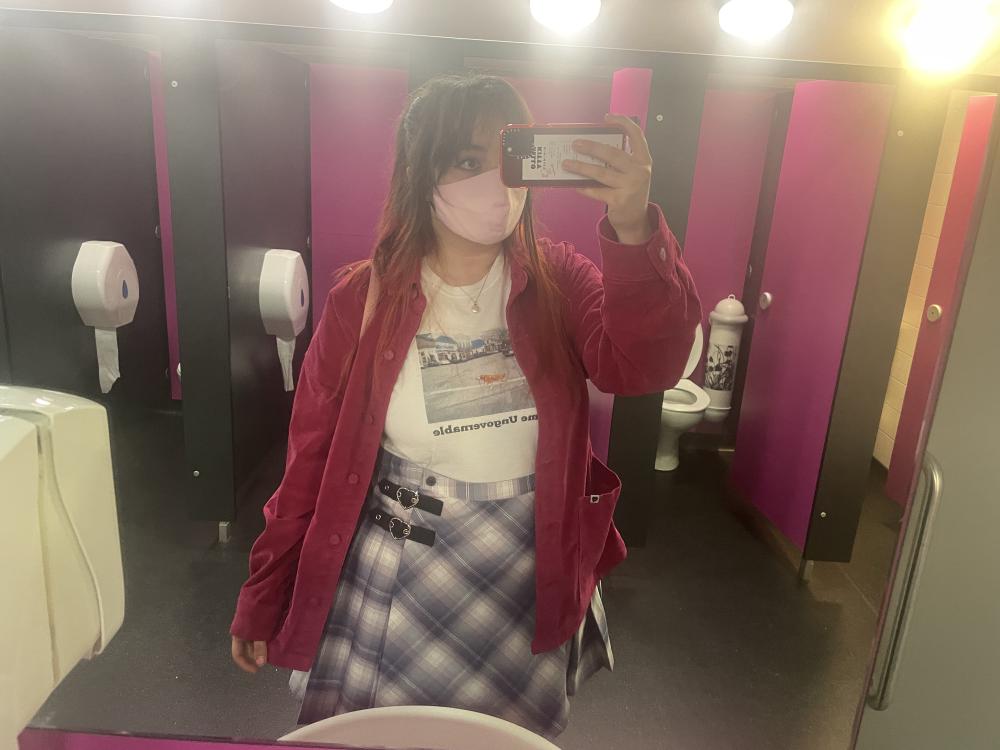 Gab takes a picture in the bathroom mirror wearing a t-shirt that says a pink cord jacket from Lazy Oaf, a lilac tartan skirt from Lazy Oaf, and a meme tshirt of a dog walking itself on a lead that says 'become ungovernable'