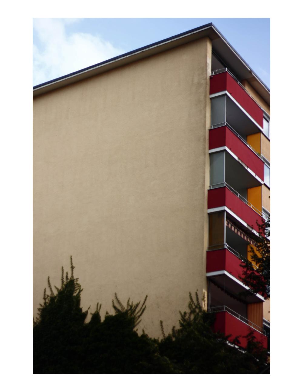 the corner of a building in berlin shows balconies in a stack with a deep red colour slanting down