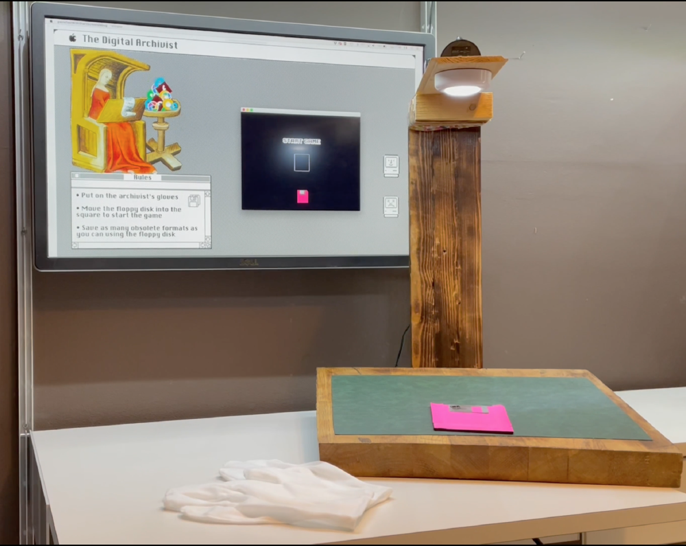 a tv screen shows the game the digital archivist while on a green block in front of it, which is under a light, there is a pink floppy disk that can be slid around for the controller, plus a pair of white gloves for the player to wear