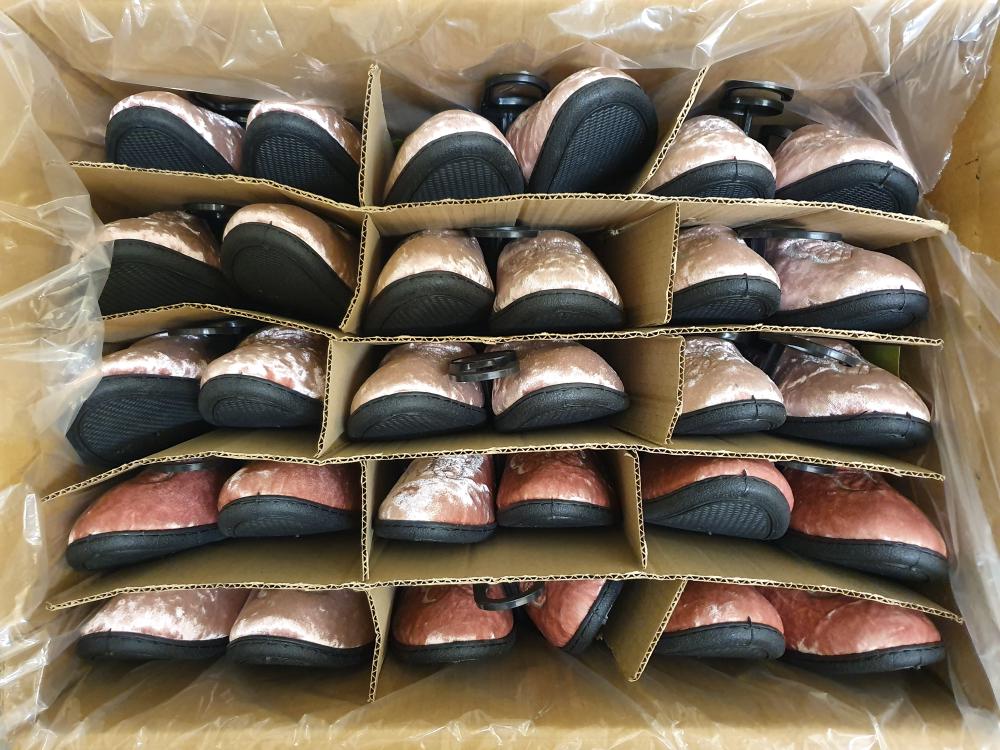 a box of pink velvet slippers in rows of pairs ready to be stocked on a shop floor