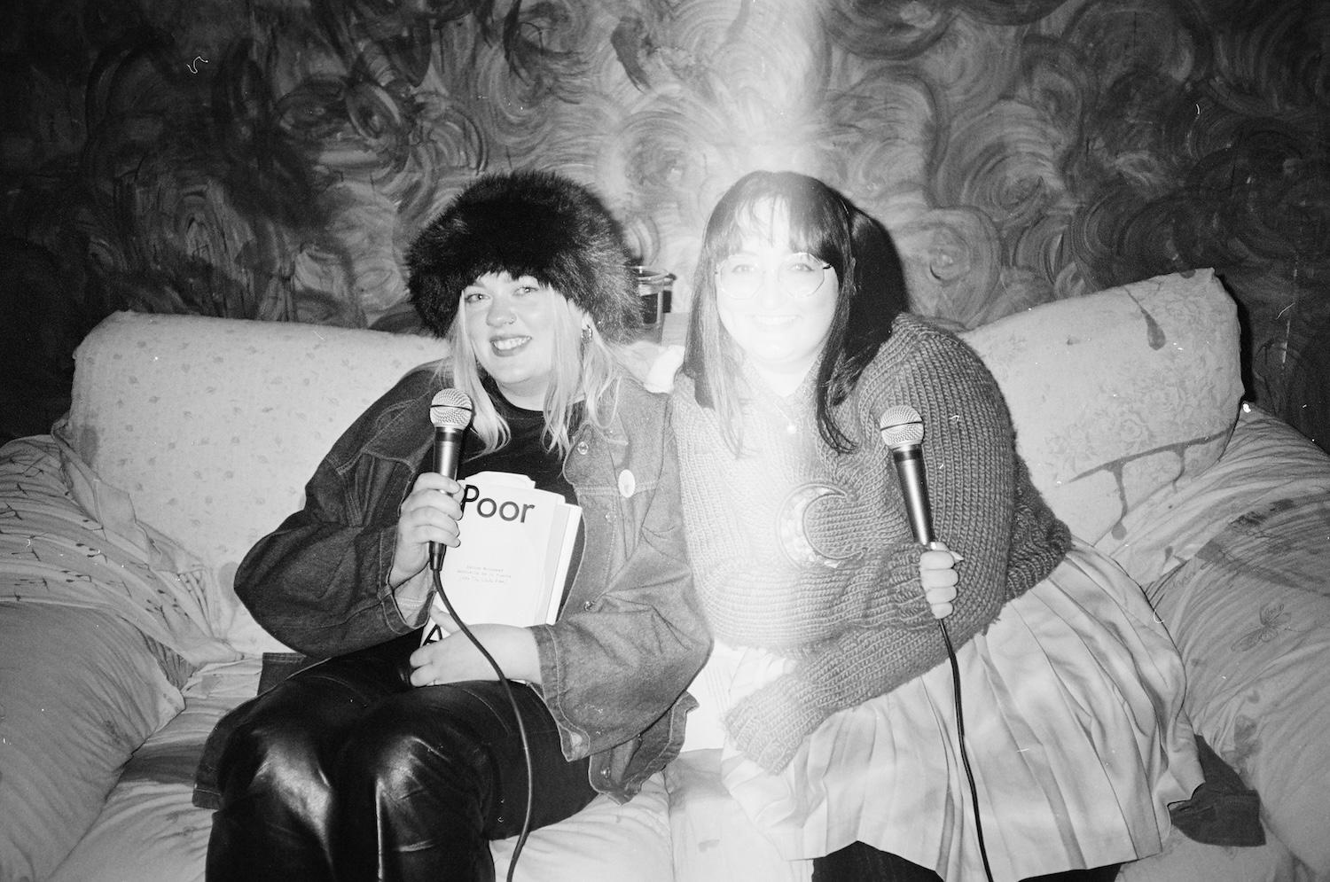 gab and laura mcsorely sat on a couch microphones in hand at the poor artists event in generator projects dundee, and laura is wearing a black fluffy hat