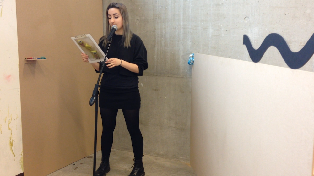 in the corner of the installation, amongst the unpainted wooden 8 by 4s, gab is reading out a piece next to a microphone