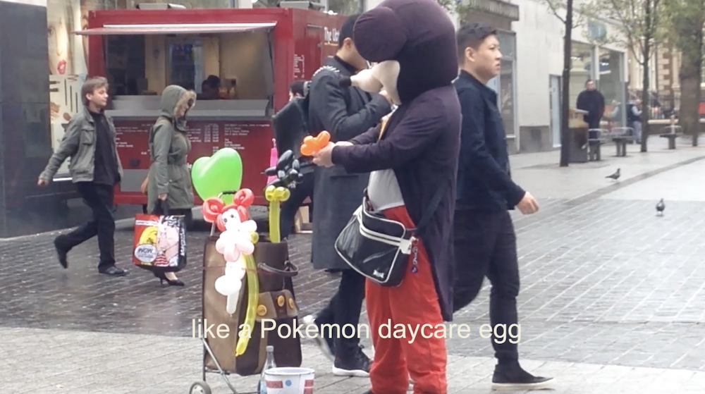 another screenshot from the video shows someone in a mickey mouse costume in the centre of liverpool making balloon animals, and the subtitles say like a pokemon daycare egg