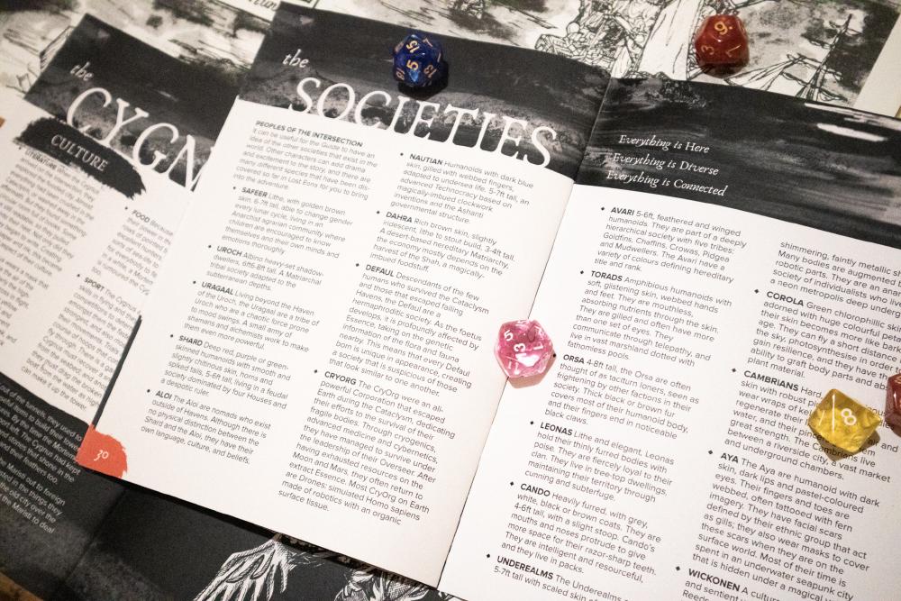 the open game booklet on a page for the societies in the game covered with colourful many-sided dice'