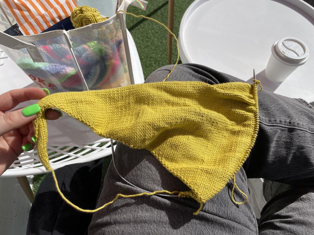 a mustard yellow neckerchief halfway through being knitted on gab's lap