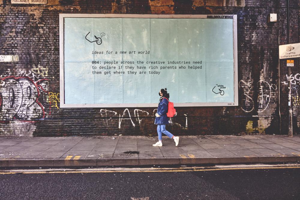 pictures of a pedestrian walking past a huge pale blue billboard that says ideas for a new art world number 4, people across the creative industries need to declare if they have rich parents who helped them get where they are today