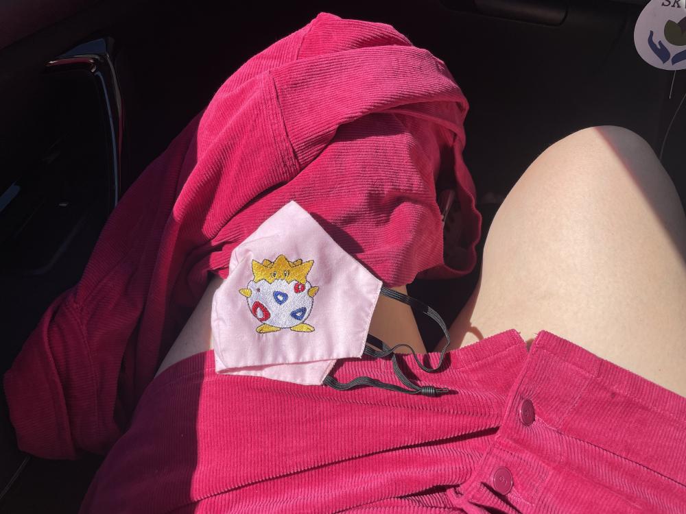my legs in a pink mini skirt with a togepi face mask on my knee in the front seat of a car