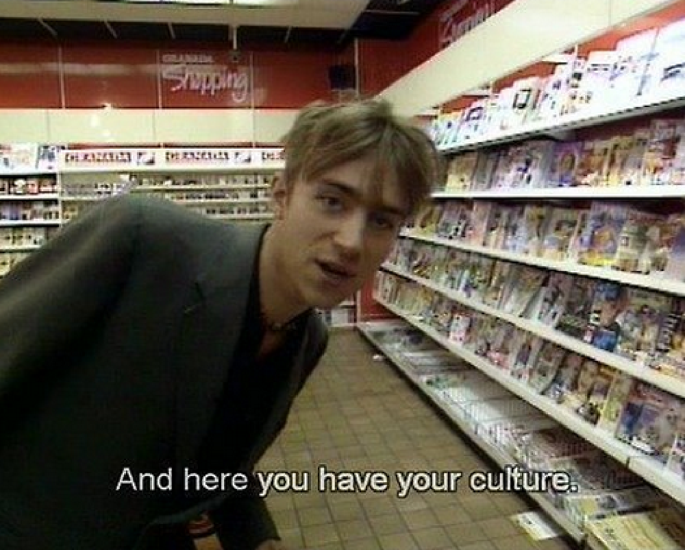 Damon albarn in a shop, in front of the magazine rack, saying: and here you have your culture