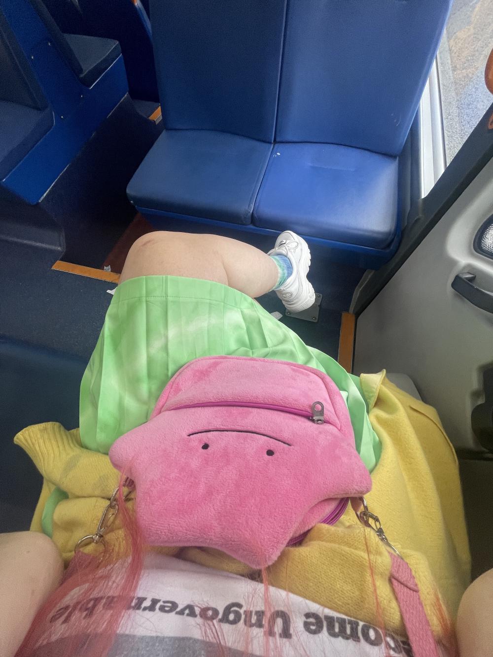 gab at the back of the bus wearing a neon green pleated skirt and a pink bag shaped like the pokemon ditto
