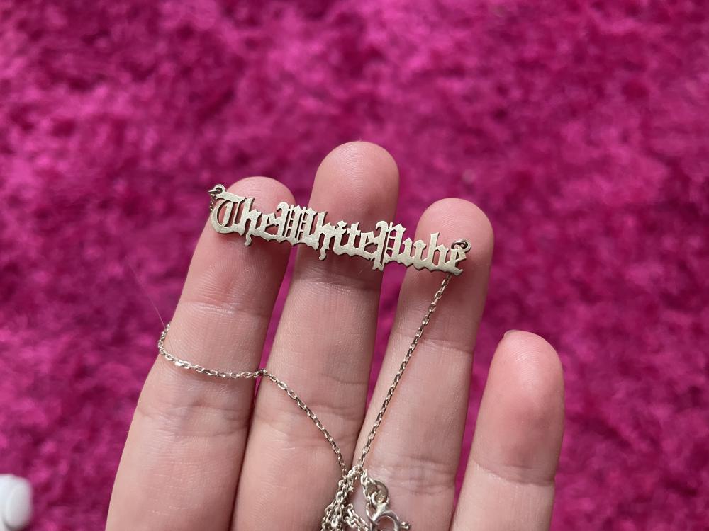 the white pube in old timey writing on a silver necklace