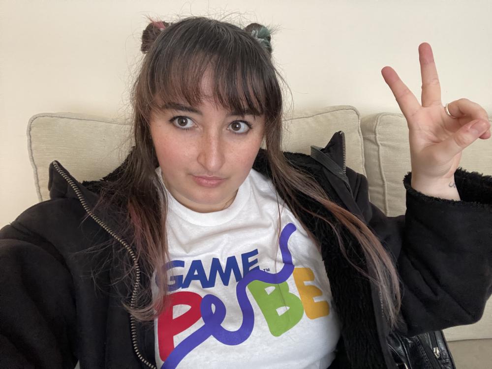 gab wearing a white tshirt with the game pube logo on it, doing a peace sign