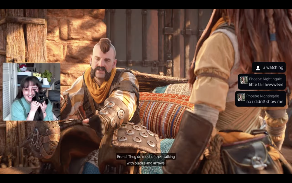 a screenshot from a horizon forbidden west screen, a few characters talking on screen one of them has an amazing moustache, all rough and ready in battle gear, and in the left hand side there's a webcam shot of gab holding here cat coco to the camera to show the audience