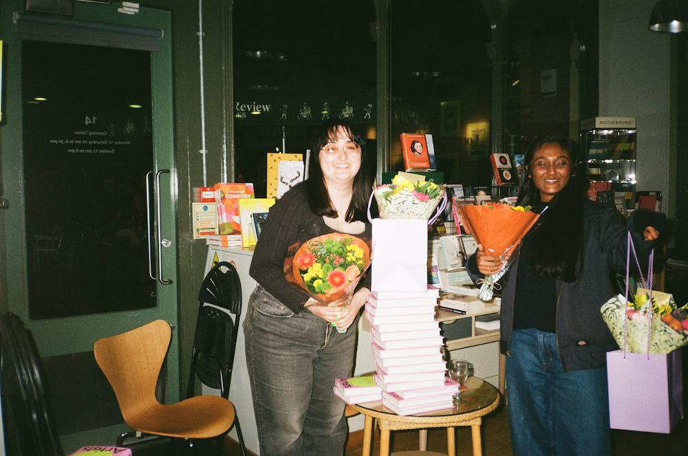 Gab and Zarina smiling with loads of flowers either side of a tower of the book