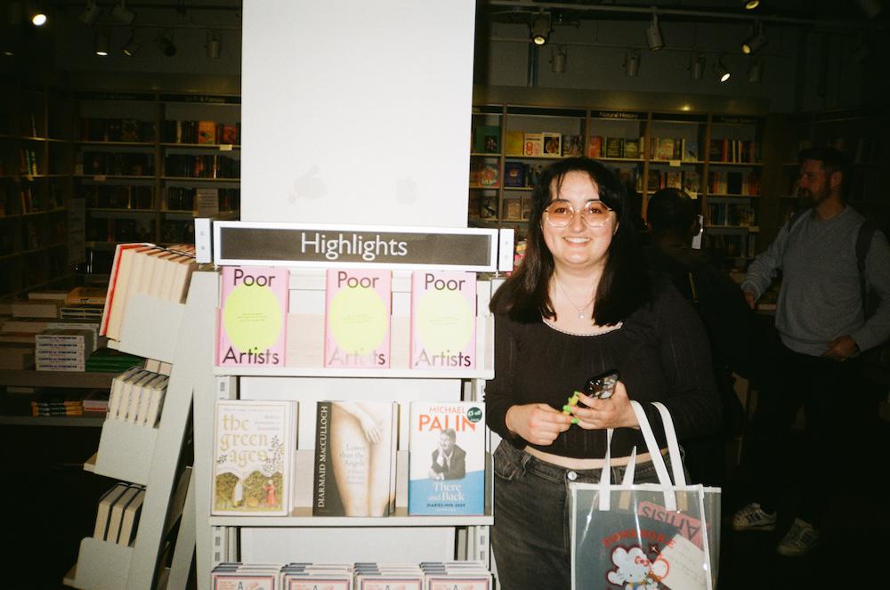 Gab smiling next to a row of Poor Artists books in the highlights section at Foyles