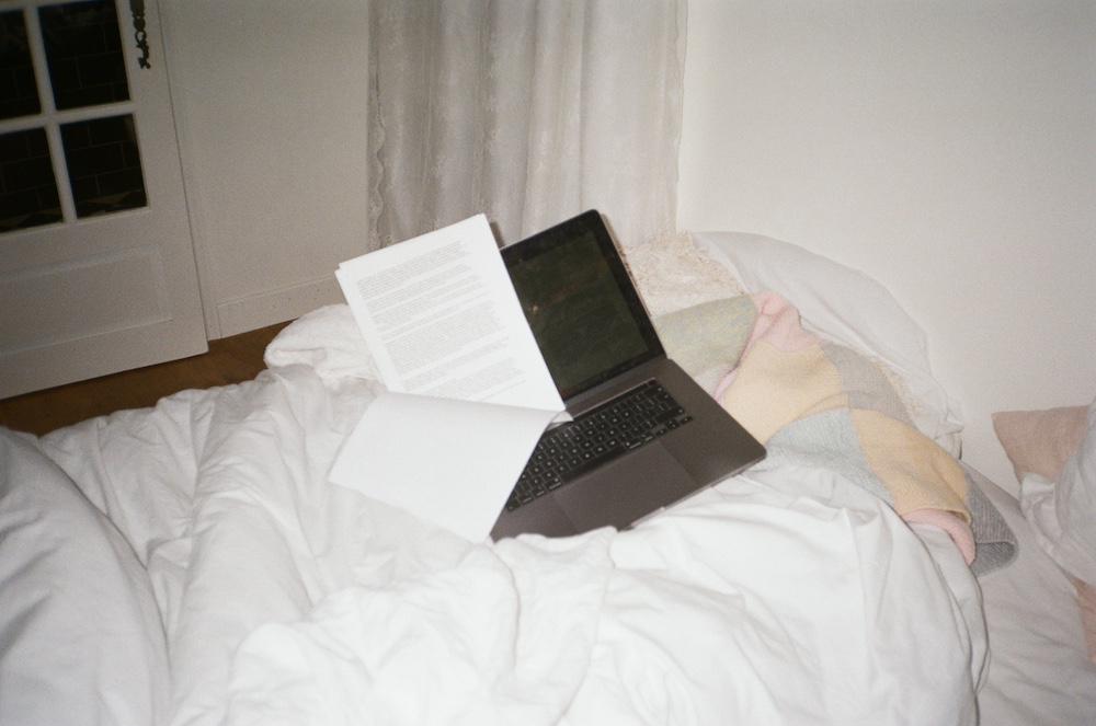 my laptop with some printed pages on the bed