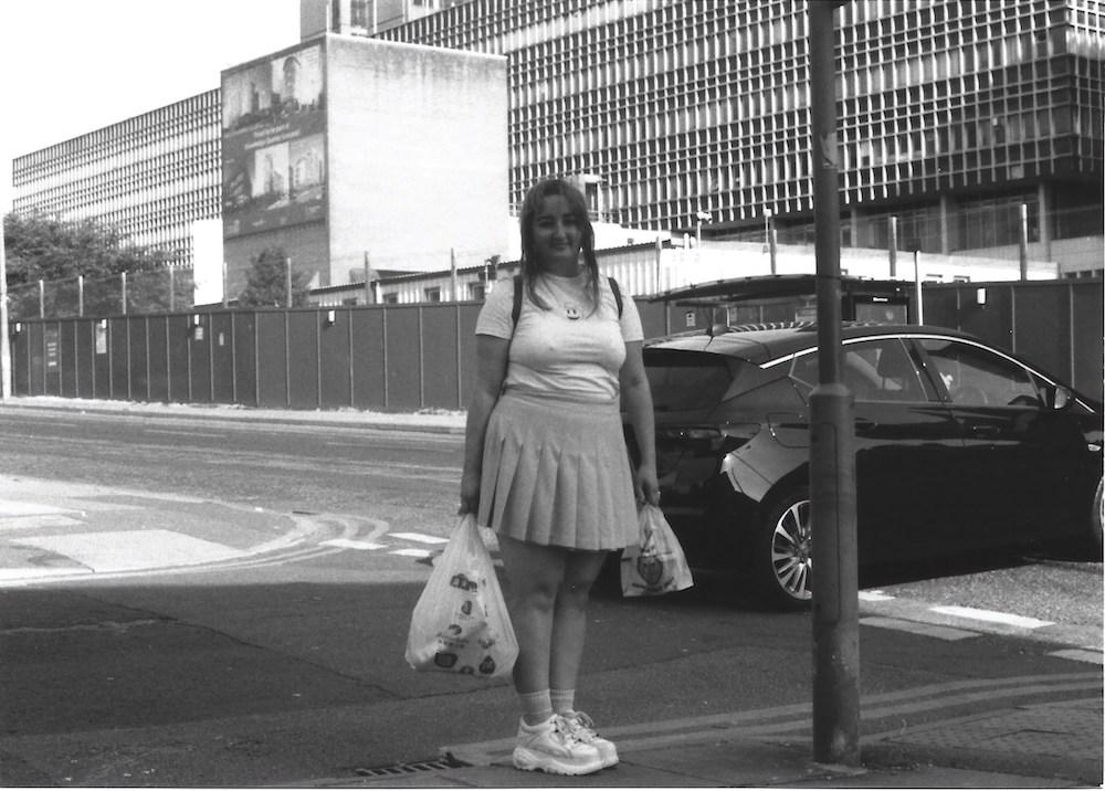 gab standing on prescot road with shopping bags, wearing a pleated scared, the old royal hospital in the background