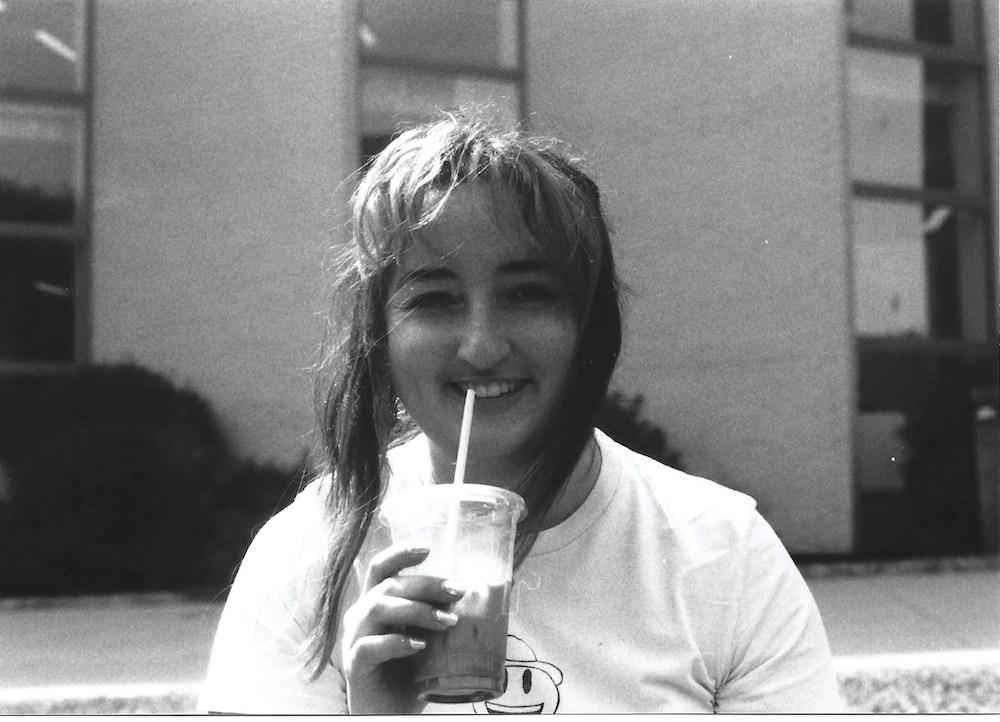 gab smiling with a matcha latte and a shirt with a cowboy emoji on it, sat outside john moores art school