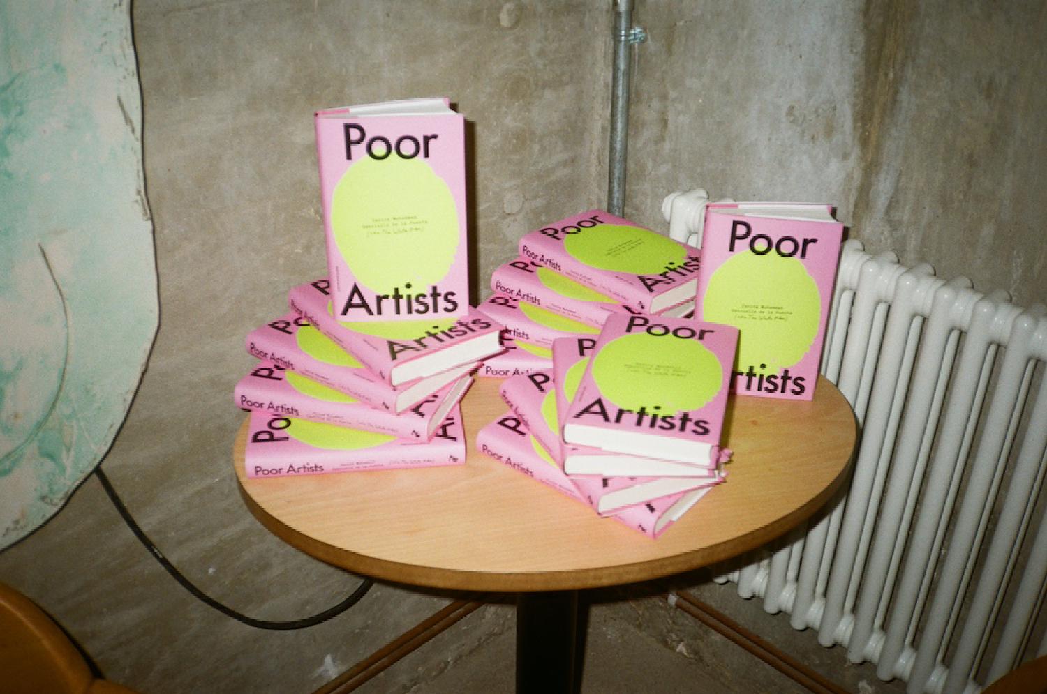 our BOOK COVER which has the title POOR ARTISTS on a bright pink background with an abstract digital painting of a lemon, featured on an artfully arranged pile of poor artist hard back books