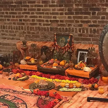 a collection of flowers and framed images and shells and tableware all arranged in a shrine on the floor