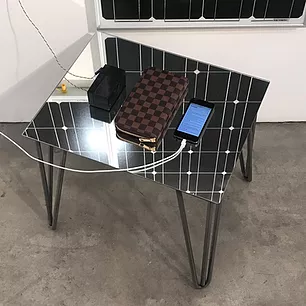a reflective table has an iphone charging and a louis vuitton checkered brown style purse next to it
