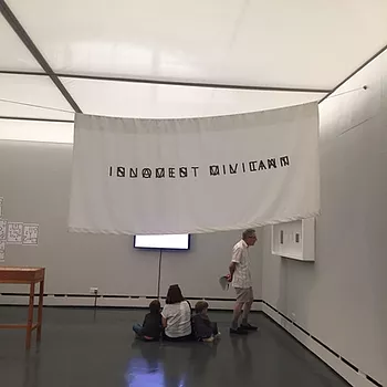 a white flag hangs over the gallery with words overlapping and unfortunately i cannot read or understand what it even says