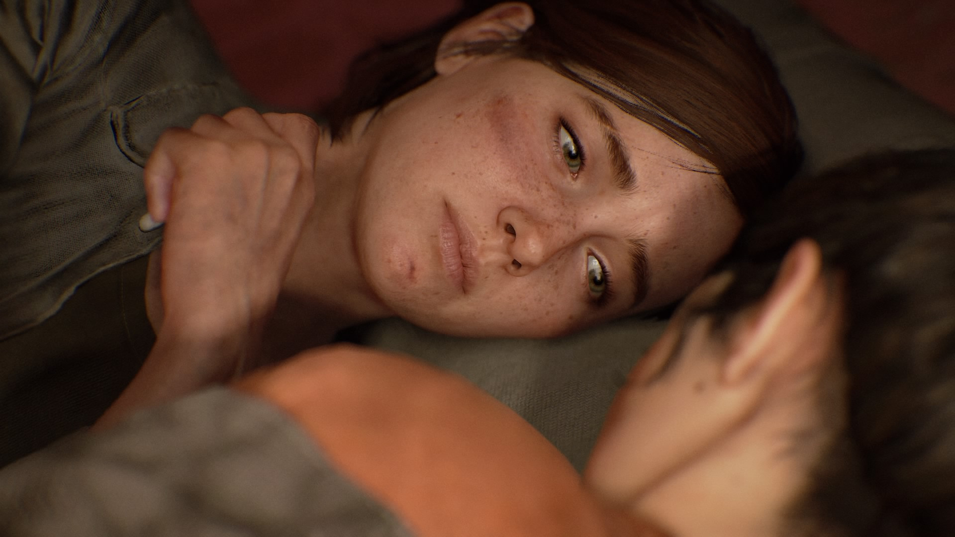 Ellie lies down close to someone whose face we can see, looking intimately at them, her face slightly bruised and sad