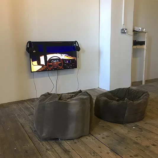 beanbags in front of a flatscreen on a wall showing the first person view of someone driving a virtual car with a wheel in front