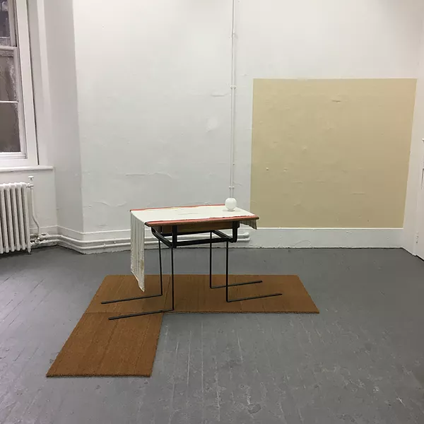 an L of wood on the floor is topped by a metal table with its legs bent outwards and straight, and on top of the table there&rsquo;s a white piece of fabric hanging over top and down at one end - plus a square of paint on one wall is coloured in beige