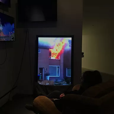 a verticle screen of a house fire, and gabrielle is sat in front watching it