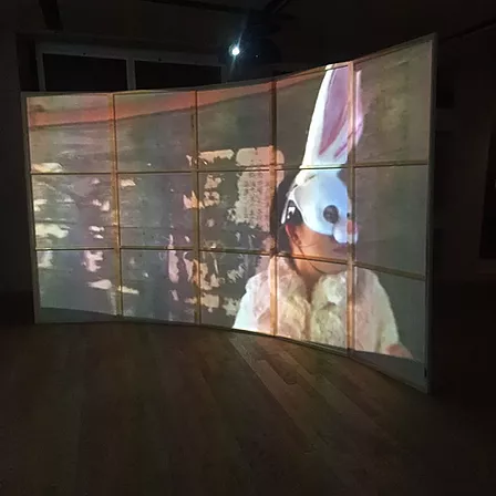 a curved projection screen shows someone looking to one side wearing a bunny mask that covers half their face and rises up into huge ears