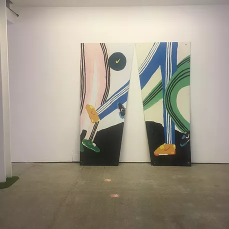 more paintings of jogger-wearing legs kicking a ball, but the painting this time is split into two halves with a big V shape cut out the button and breaking up the piece
