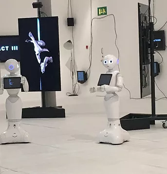 a picture of a white room populated by verticle flat screen tvs and walking robots who have tablets on their chests. The robots are quite cute looking