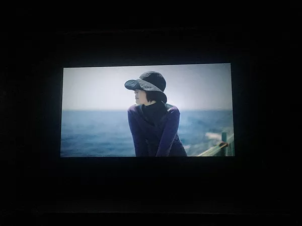 a woman in japan sits looking out of water with a black floppy hat on