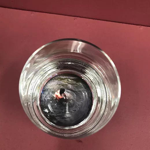 looking down into a glass with some water in it, there is an image at the very bottom of a man with no top on sitting in water
