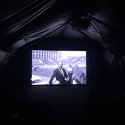 a projection in black and white of martin luther king in what looks like a football stadium