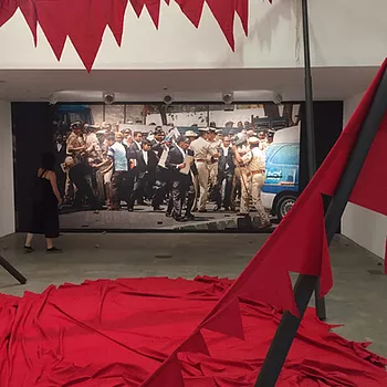 an image of a clash between a protest and the police, and a big red fabric piece on the floor in front of it with spikey edges