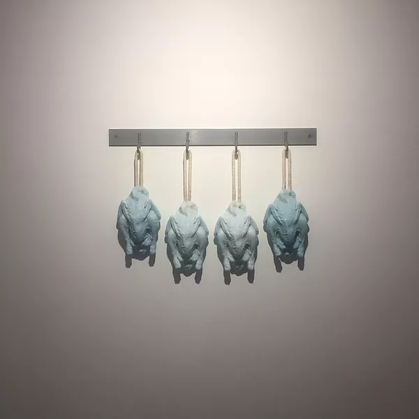 four blue sculptures of skinned chickens hanging from a row of hooks on the wall