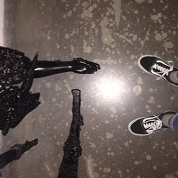 zarina takes a photo looking down at her shoes and at a sculpture opposite her, like theyre taking a shoe picture together