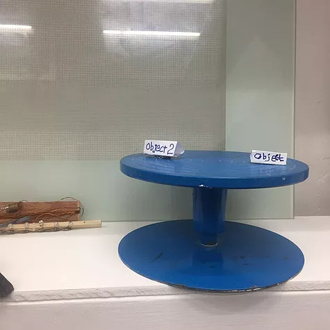 a blue cake stand in a vitrine has two pieces of paper on it saying object and object 2