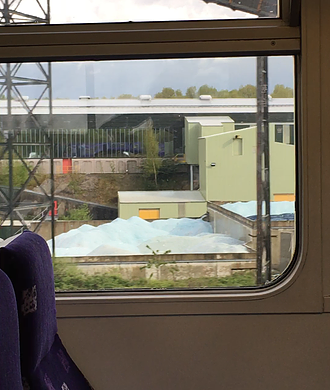 a shot out of the train of a factory with piles of what looks like broken glass, a slight pale blue