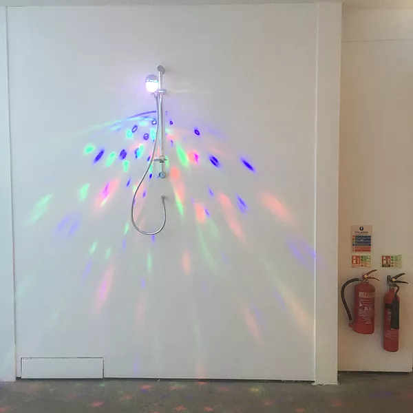 there is a shower mounted on the wall and where the water would come out, a tiny clear disco ball that casts out fun colours in a big triangle down the wall, replacing water with colour and light