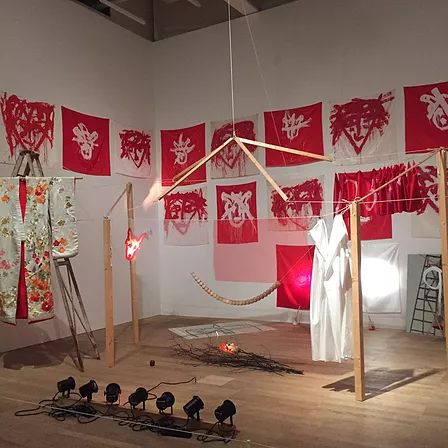 a corner of an exhibition space full of white and red faces painting in an abstract style, and in front of the wall, there are wooden sticks and strings holding each other up