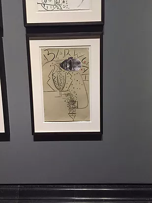a framed drawing is hung on a wall showing a drawing of a man&rsquo;s suit jacket but there&rsquo;s a photographic head stuck on top